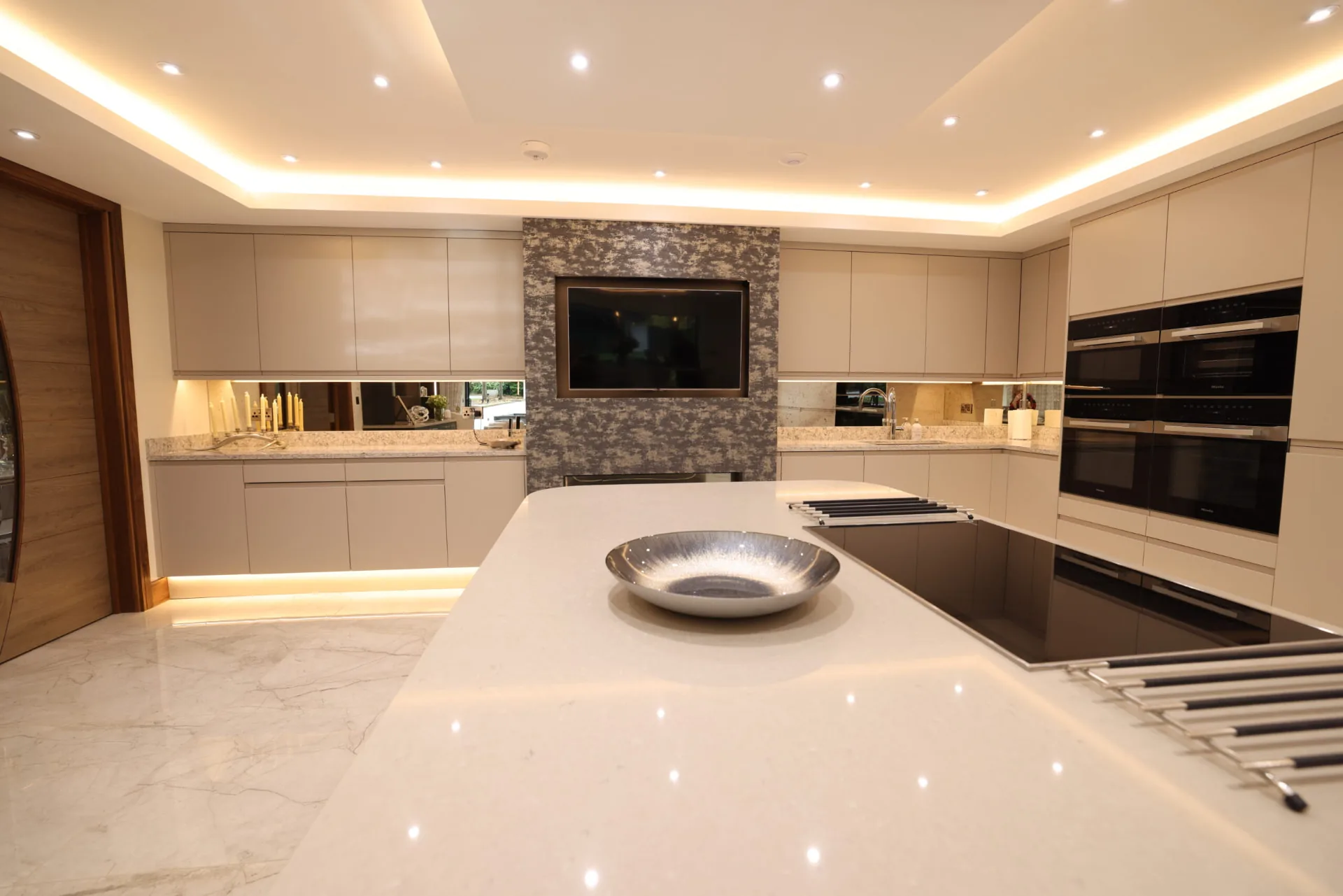 Open-plan kitchen island with a marble worktop and feature media wall