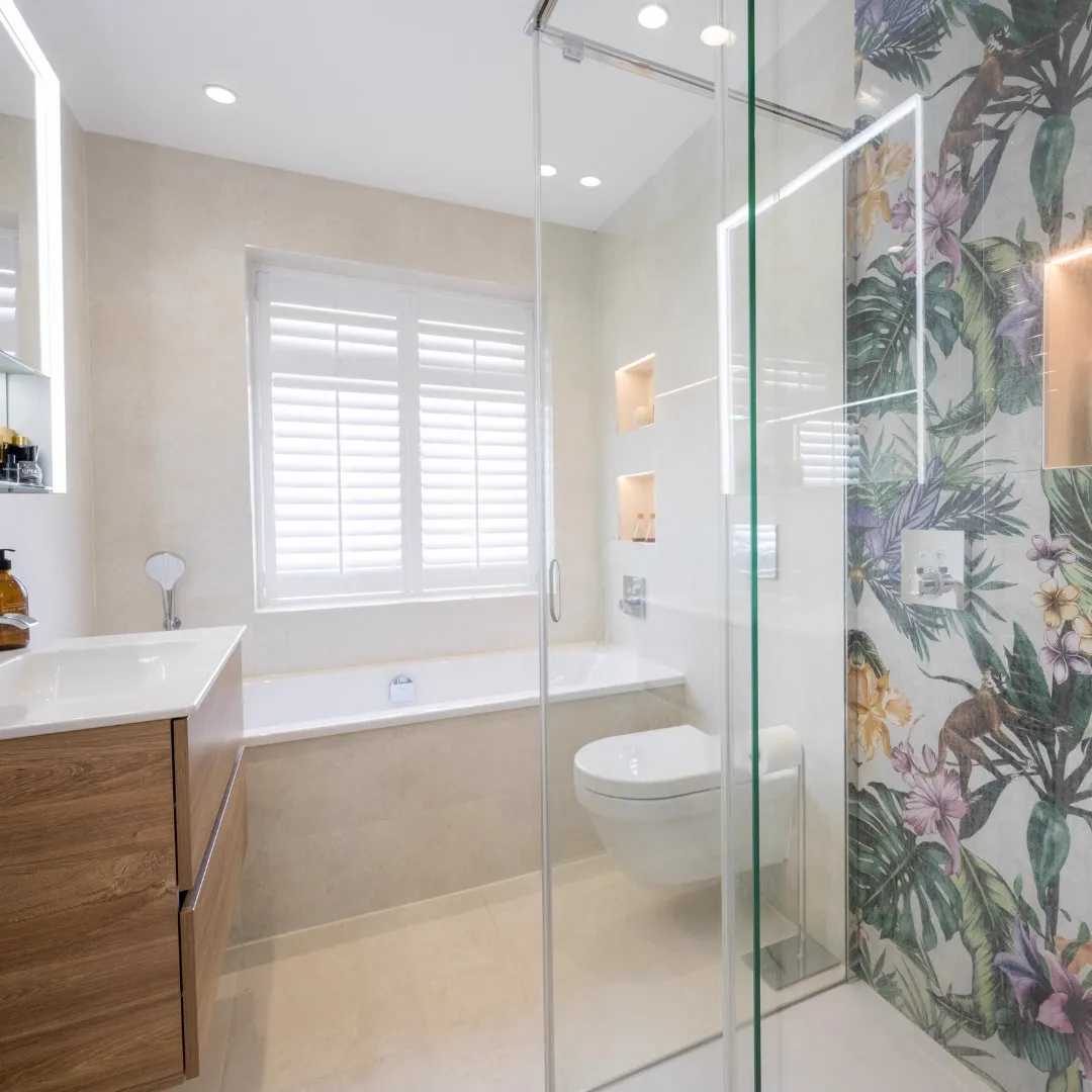 Bathroom with a tropical-print feature wall in the shower, a timber-effect vanity, a fitted bath and shuttered window