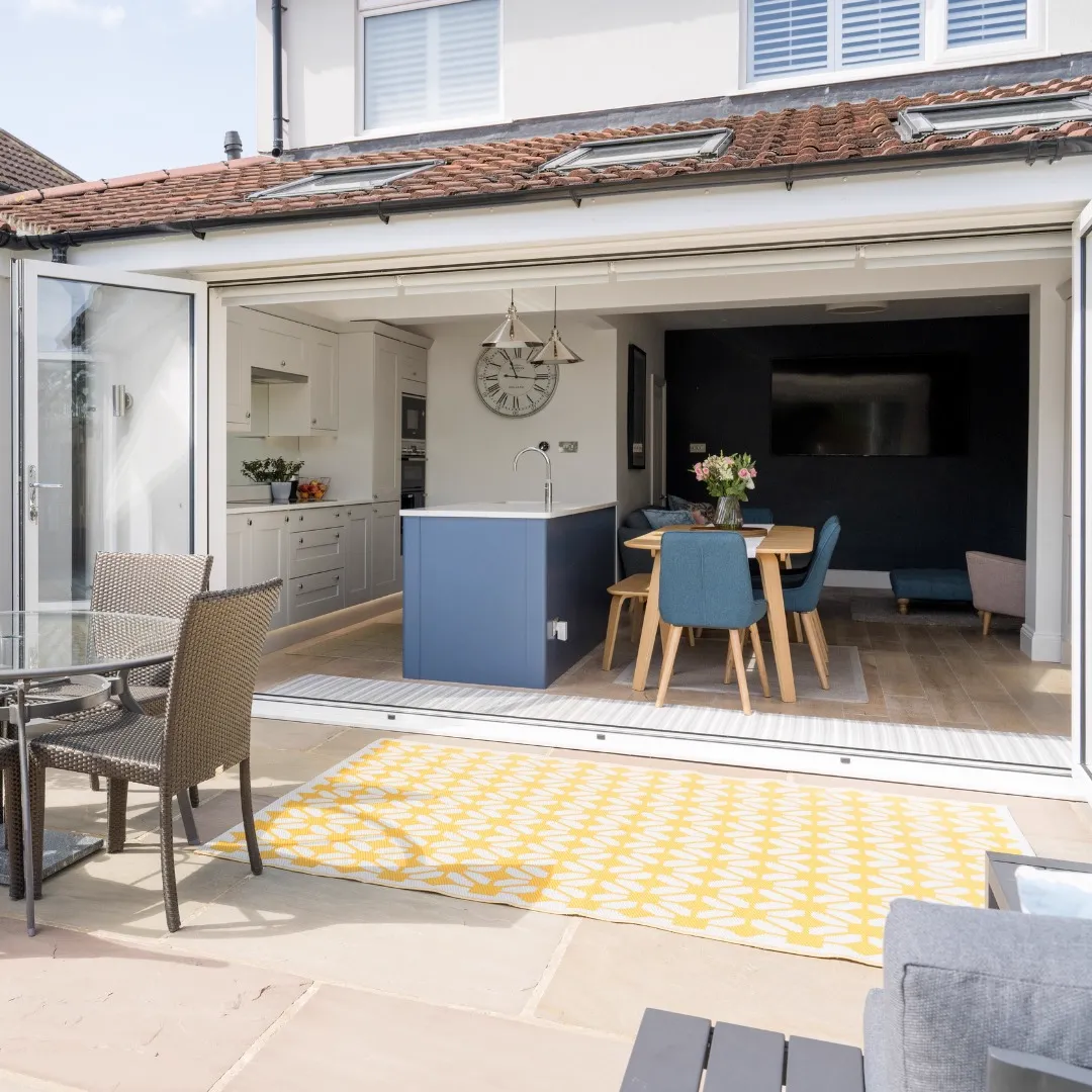 View from the patio through fully open bi-fold doors into the kitchen, dining area and a dark-walled living space