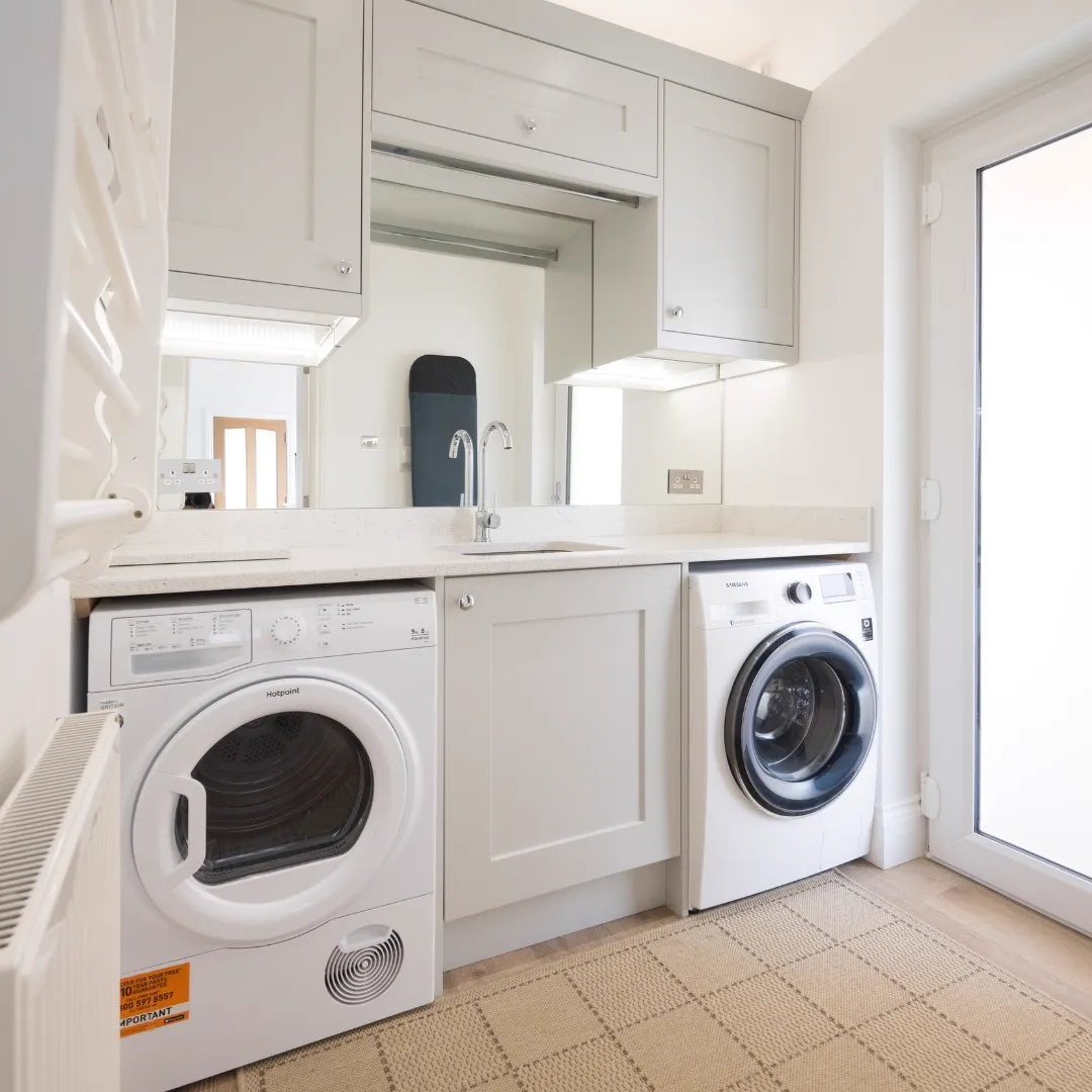 Utility room with grey shaker cabinets, a pale worktop with sink, a tumble dryer and washing machine beneath, and a glazed door