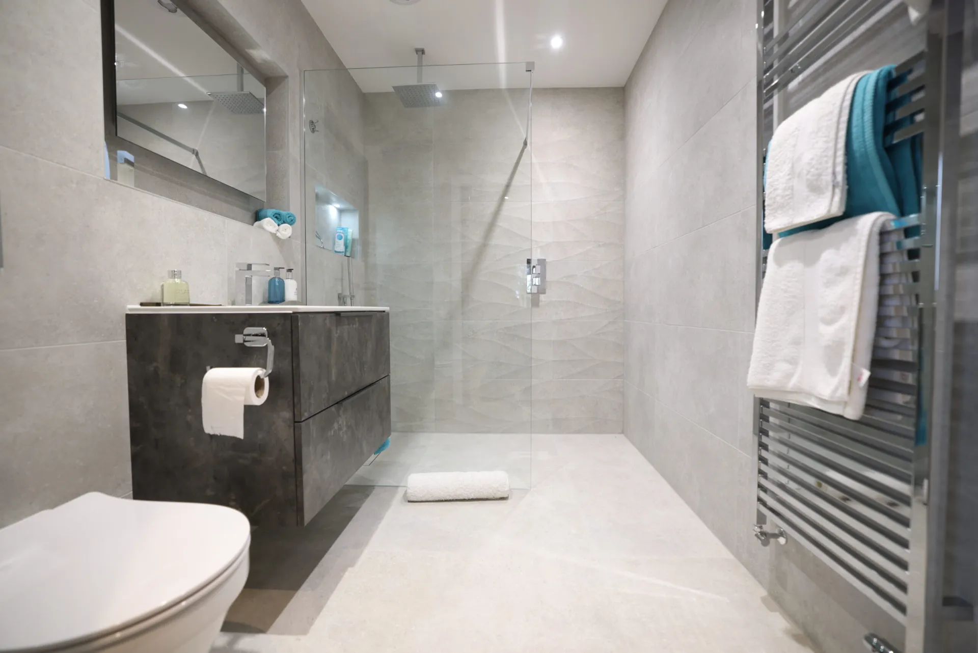 Grey-tiled shower room with a walk-in glass screen, textured feature wall and a chrome towel radiator
