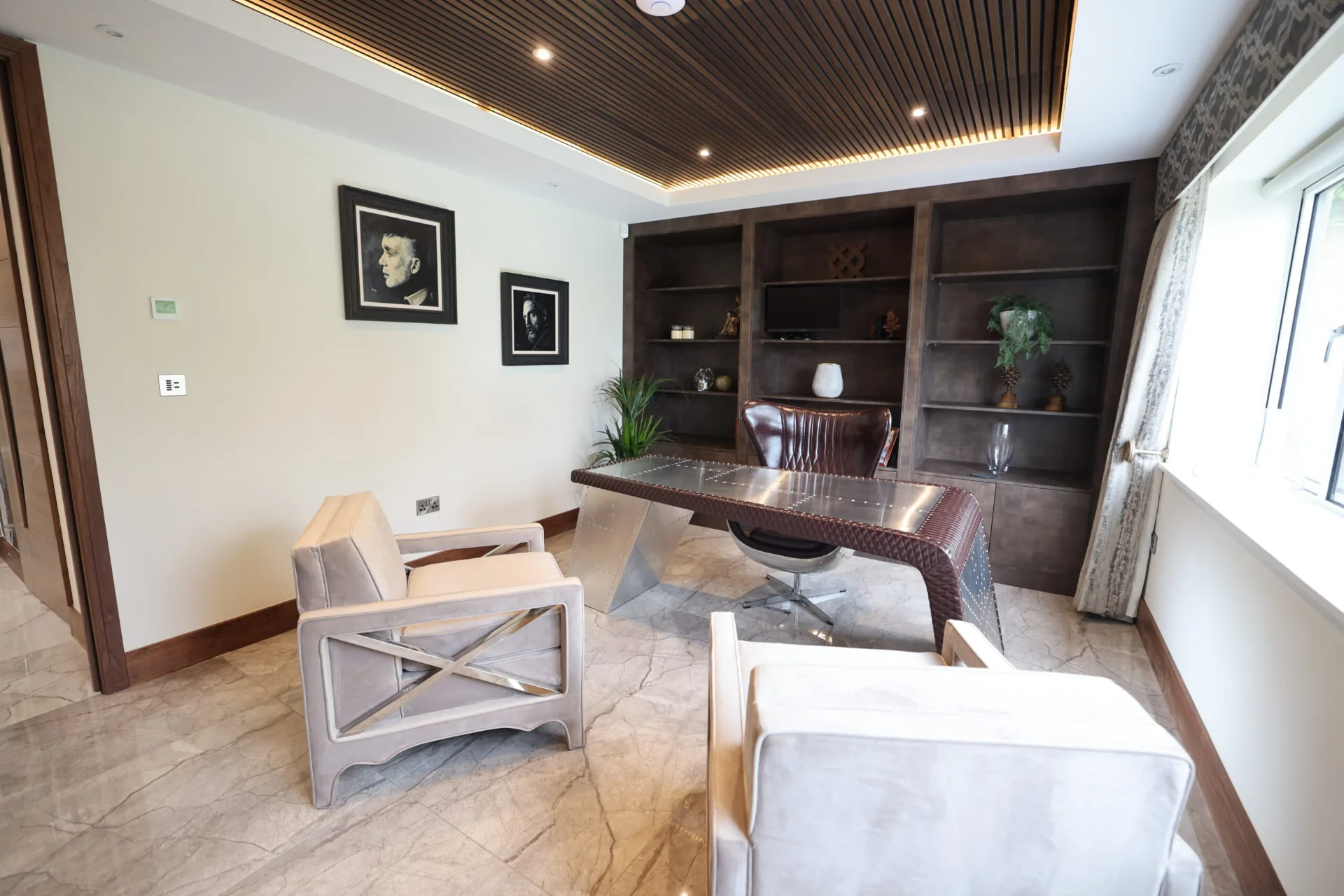 Home office with dark timber joinery, a slatted wooden ceiling, an aviation-style desk and leather seating
