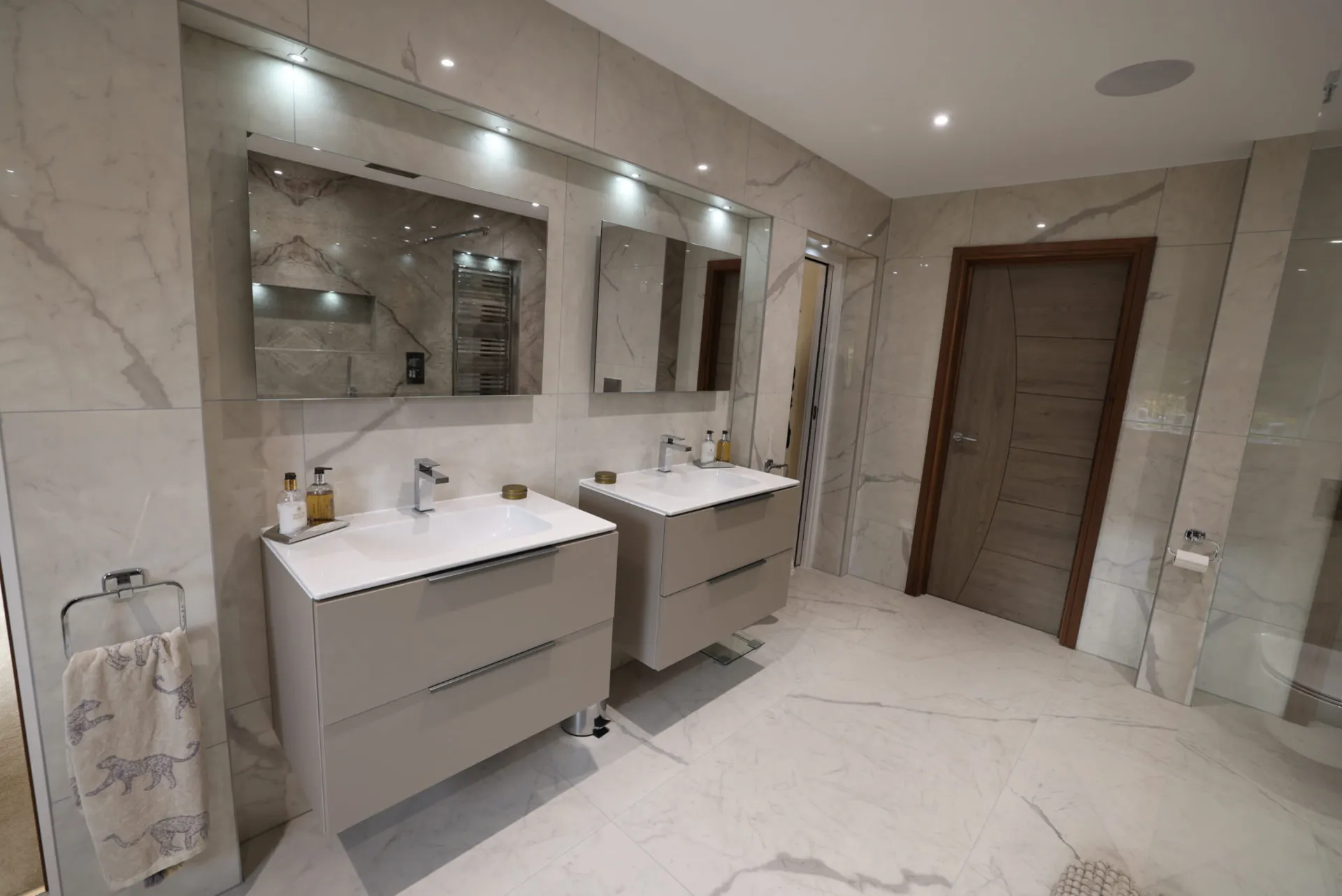 Twin wall-hung vanities beneath lit mirrors in a marble-effect master bathroom