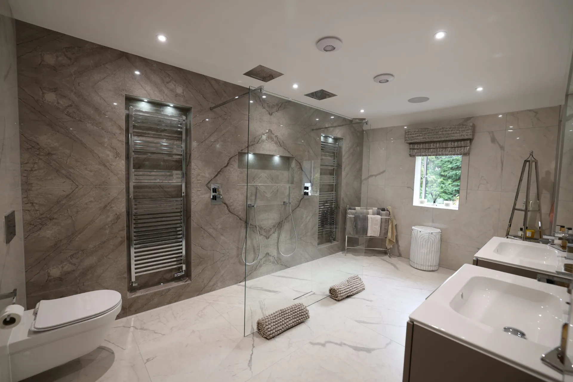 Master bathroom with a book-matched stone-effect feature wall, twin-head walk-in shower, recessed towel radiators and twin vanities