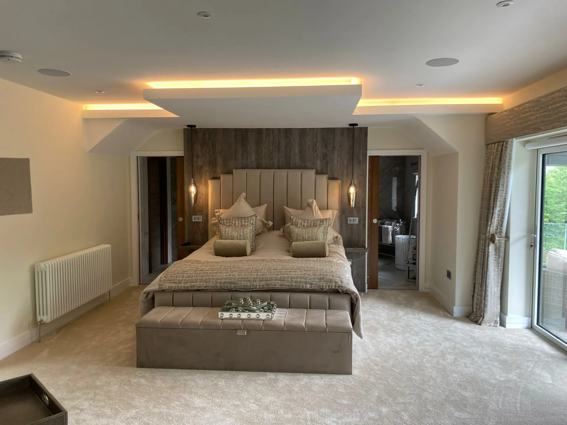 Bedroom with an upholstered headboard set against a timber-effect wall, pendant lights and a lit dropped ceiling