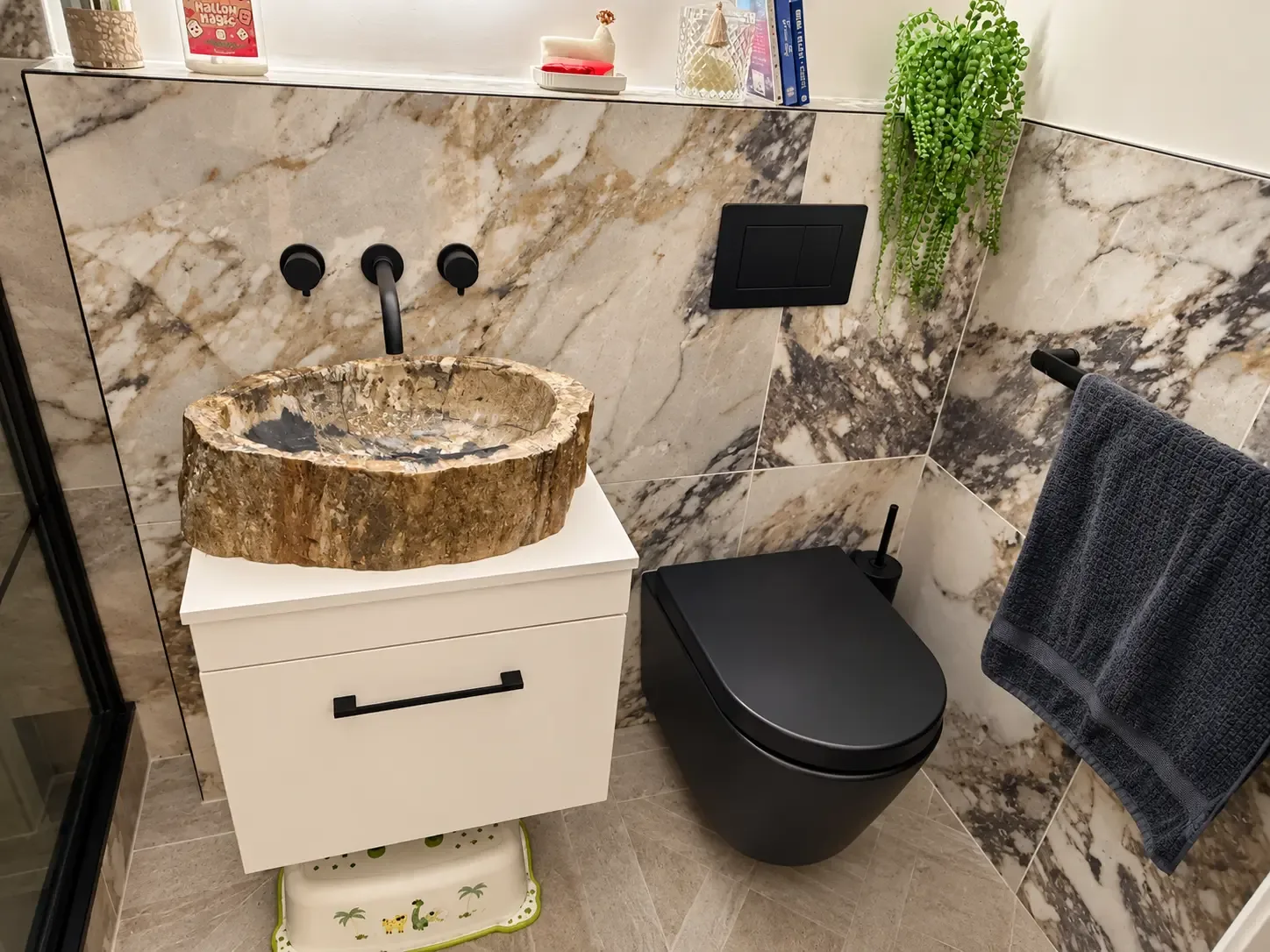 Downstairs WC with bold veined stone-effect tiles, a stone vessel basin on a white vanity, black wall-mounted taps and a black wall-hung WC
