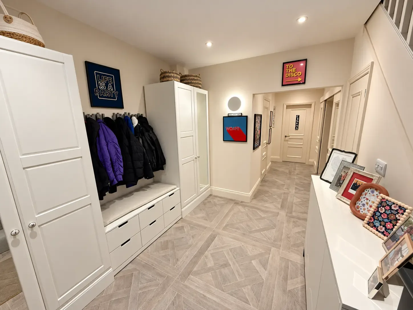 Hallway with white fitted cupboards, a coat area with bench and drawers, and a patterned wood-effect floor leading to further rooms